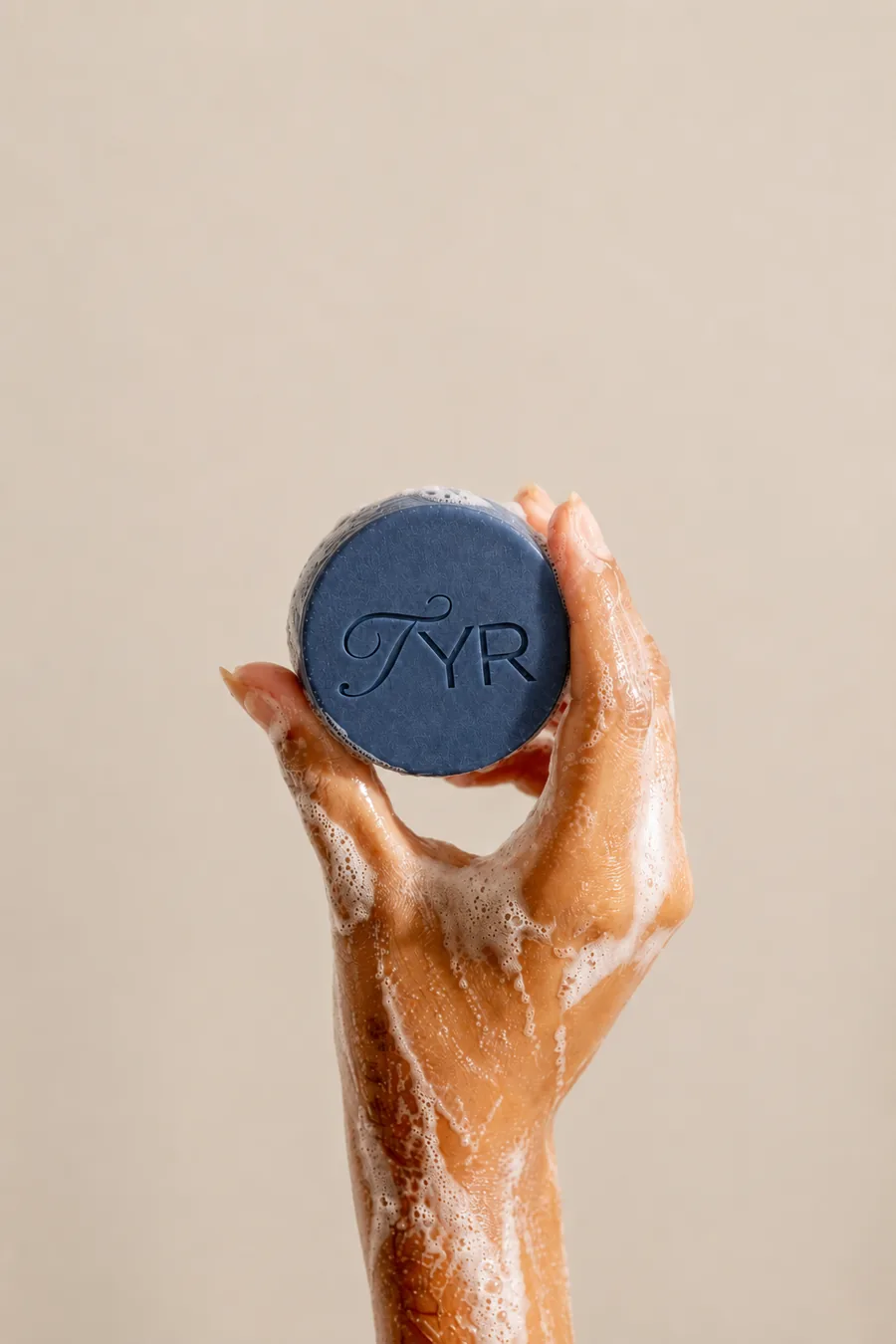 Tangan berbusa mengangkat sabun batang Treat You Right berwarna navy dengan emboss TYR.